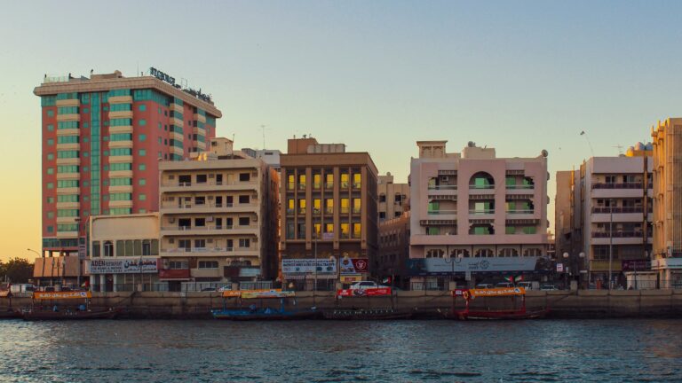 Old Dubai walking tour — traditional abra boats on Dubai Creek at golden hour, with weathered Deira-side shopfronts in the background